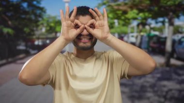 İspanyol adam gülümser ve yoğun bir şehir caddesinde dururken gözlerinin üzerinde el dürbünü oluşturur; eğlenceli bir keşif.