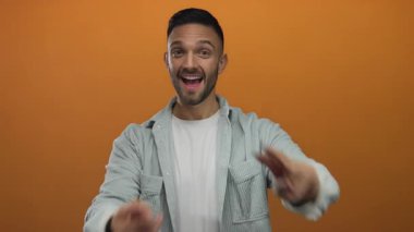 Genç adam canlı turuncu arkaplan, coşkulu ifade gösteren hashtag sembolü, kot gömlek ve beyaz tişört giyerek gündelik stil