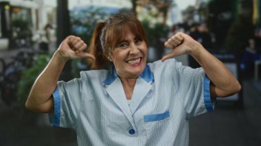 Üniformalı kıdemli İspanyol kadın hareketli bir şehir sokağında dikilirken kendine güvenerek gülümsüyor. Temizlik mesleğiyle gurur duyduğunu söylüyor..