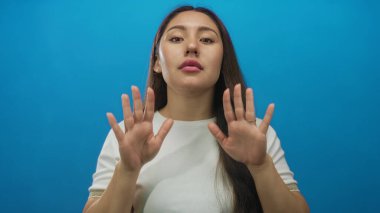 Genç İspanyol kadın düz, canlı, mavi stüdyo duvarına karşı el hareketlerini durdurmak için avuçlarını kaldırıyor..