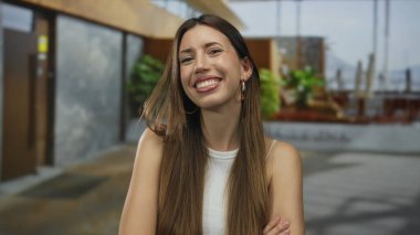 Çapraz kollu genç İspanyol kadın modern bir bina girişinde kolsuz bluz giyiyor..