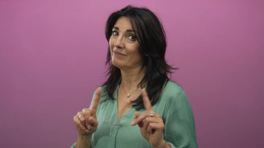 Yeşil bluzlu kadın, pembe stüdyodaki kameraya işaret ediyor ve yasaklanmış bir bakış atıyor..