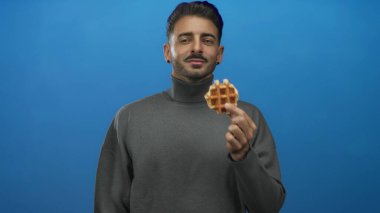 Stüdyoda waffle koklayan bir adam gri balıkçı yakalı, gözleri kapalı ve kurnaz bir gülümseme takınıyor..