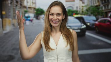 Beyaz kolsuz bluzlu genç bir kadın güneşli bir şehir caddesinde havaya bir öpücük yolluyor..