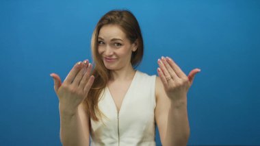 Parlak mavi bir stüdyo duvarının önünde uzanmış elleri olan genç bir kadın davet ediyor..