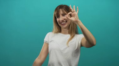 Stüdyoda sağ elinle işaret dilini gösterirken ayakta duran ve gülümseyen kadın, sevinç onayı..