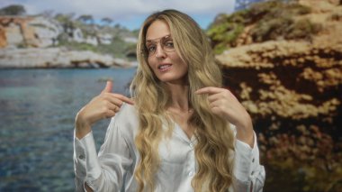 Kadın, kumsalda genç sarışın figürünün yanında el pençe divan duruyor. Karşılama jesti ile odak noktasını arıyor..