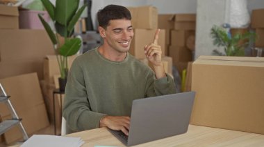 Karton kutularla çevrili bir binanın içinde dizüstü bilgisayarda yazan adam, düşünceli bir planlama..