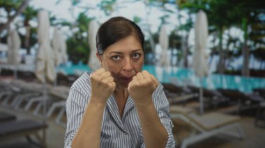 Orta yaşlı bir kadın açık havuz kenarında çizgili gömlekle yumruk atıyor. Kararlılık..