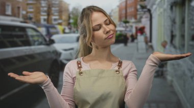 Önlüklü kadın, kalabalık bir şehir kaldırımında omuzları açık bir şekilde ayakta duruyor; şaşkınlık şüphesi belirsizlik belirsizliği belirsizlik tereddüdü, soru ikilemi, karşılaştırma.