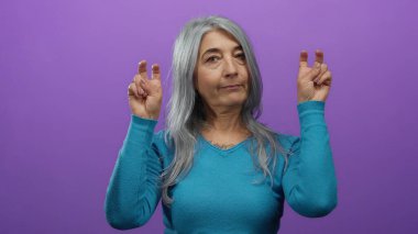 Yaşlı gri saçlı kadın, sakin bir ifadeyi gösteren izole bir mor arka plana karşı barış işareti yapıyor..