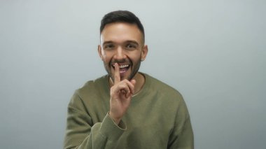 Sıradan bir eşofman altı giyen genç adam parmakları beyaz arka planda olan dudaklarıyla şşşş hareketi yapıyor. Sessizliğini ya da gizliliğini neşeli bir gülümsemeyle ifade ediyor..