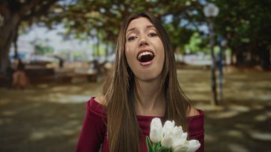 Gündüz vakti açık gökyüzü altında beyaz laleler tutan ve göğsüne dokunan bir kadın..