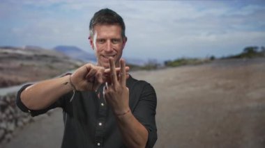 Taş duvarlı bir yolda ellerini sayarken üç parmağını gösteren adam, özgüvene odaklan..