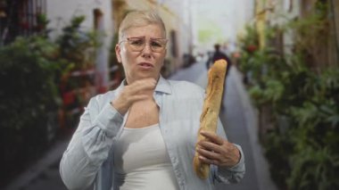 Dar bir şehir caddesinde, elleri havada, uzun bir baget tutan orta yaşlı kadın, vurgu için gözlük ve açık gömlek giyiyor; sert reddetme.