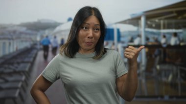 Kadınlar başparmağıyla güvertedeki tırabzanları işaret ederken gülümsüyor ve yana bakıyor; oyuncu özgüven.