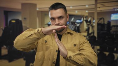 Spor salonunda elleri spor aletleri ve dambıllarla kaplı bir mola tabelası yapan bir adam..