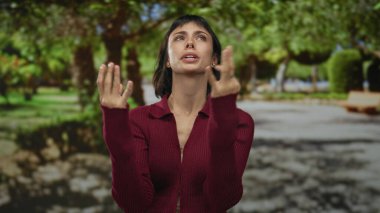 Kırmızı kazaklı İspanyol kadın, gün ışığında kollarını kavuşturur ve kaşlarını çatar. Gergin duruşuyla, öfke hüsranı meydan okumasıyla..