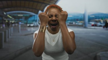 Havaalanı terminalinde elleri havada ve ağzı açık genç Afro-Amerikalı kadın. Heyecan verici..