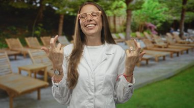 Laboratuvar önlüğü giyen ve gözlük takan kadın bilim adamı çimenlikte ahşap şezlonglarla ormanda şans diliyor..