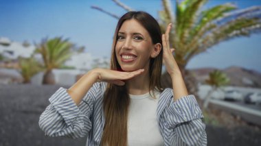 Gülümseyen ve sokakta elleri çizgili palmiye ağaçları ile kaplı çerçeveli kadın; neşe neşe neşesi neşe.