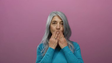 Mavi kazaklı yaşlı kadın pembe bir arka plana öpücük yolluyor jesti ve yüz ifadesiyle sıcaklığını ve sevgisini iletiyor..