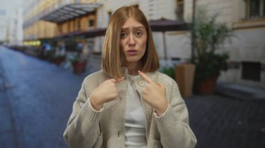 Sokakta göğsünü işaret eden genç sarışın kadın ve kafası karışmış ifade; kendinden şüphe eden kafa karışıklığı..