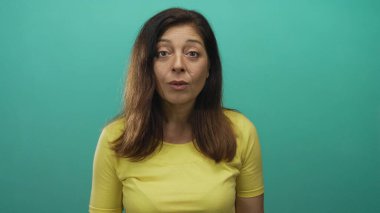 Stüdyo ortamında elleri havada, orta yaşlı İspanyol bir kadın, sarı gömlekli, sürpriz..