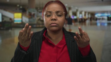 Kırmızı tişörtlü ve gözlüklü kadın, yoğun havaalanı terminalinde iki eliyle 