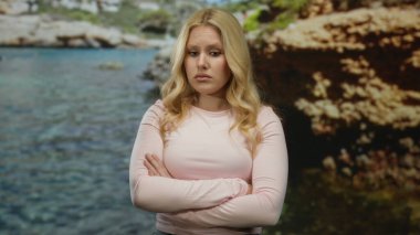 Deniz meltemi sarı saçlarıyla okyanusun dingin zeminine ve kayalık kıyılarına vururken düşünceli bir şekilde kumsalda duran bir kadın..