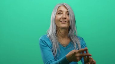 İzole edilmiş yeşil arka plan duvarına işaret eden gri saçlı yaşlı kadın modern iletişim ve sosyal etkileşimi somutlaştırıyor..