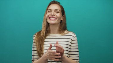 Genç Kafkas kadın geniş bir gülümseme içinde bir deniz mavisi stüdyosunda nazik bir ritimle el çırpıyor; sevinç destek alkışlarını kutluyor.