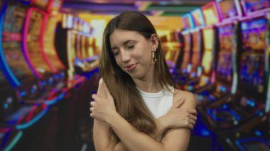 Kumarhane binasında renkli bir kumar makinası reyonunda kendine sarılan genç bir kadın..