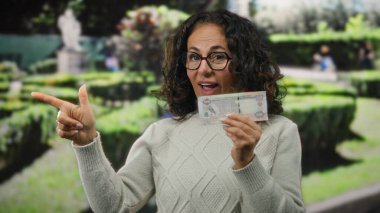 Parkta orta yaşlı bir kadın elinde Uae Dirham banknotu tutarken heyecanla işaret ediyor..