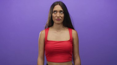 Omuzları açık bir kadın mor stüdyo ortamında nötr bir ifadeyle yukarı bakıyor; düşünceli..