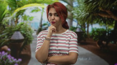 Yeşil gölgelik altında görünen kolları ve kol saati ile orman yolunda kadın çene üzerinde el; düşünceli yansıma.