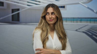 Kadın ön kolunu tutuyor ve terasta yan yana bakıyor; tefekkür yansıması.