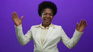 Beyaz takım elbiseli bir kadın canlı mor bir arka plana gülümsüyor, mutluluk ve profesyonellik sergiliyor, ellerini canlı bir şekilde kaldırıyor..