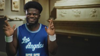 Mavi basketbol formalı bir adam müze binasında bileklik takıyor, kameraya gülümsüyor, umut verici bir merak içinde..