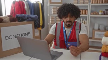 Binanın içinde dizüstü bilgisayar kullanırken kredi kartı tutan gönüllü bir adam; topluluk şefkat yardımını destekliyor.