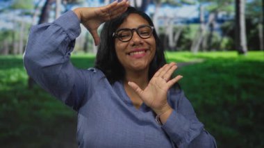 Gülümseyen Afrikalı Amerikalı kadın, güneş ışığı altında ormanda elleri ile yüzünü çerçeveler.
