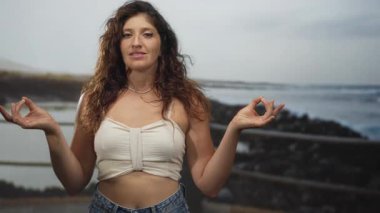 Meditasyon yapan bir kadın el hareketi ve deniz kenarındaki korkuluklarda çıplak göbek bağı; dinginlik..