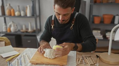 Sanatçının stüdyosundaki masada çıplak elle kil şekillendiren adam, odaklanmış yaratıcılık adanmışlığı..