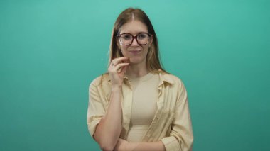 Stüdyoda düşünmek için elleri çenesinde yuvarlak kollu ve gözlüklü bej gömlekli kadın; sessiz tefekkür.