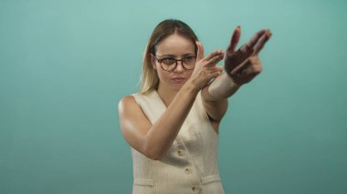 Stüdyoda bir silah gibi parmağıyla kamerayı işaret eden kadın turkuaz duvar ve bardaklar görünür, kararlılık odaklı..