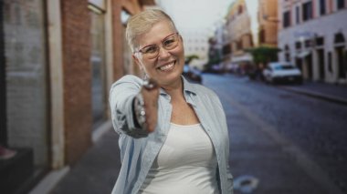 Kadın kaldırımlı bir şehir caddesinde el sıkışmak için sağ elini uzatıyor, gülümsüyor ve kameraya doğru uzanmış bir şekilde öne eğiliyor; samimiyet güven bağlantısı.
