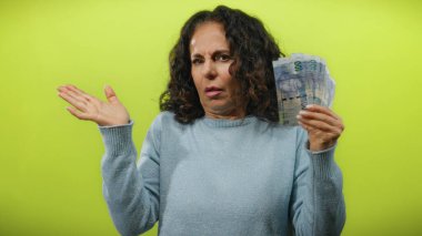 Orta yaşlı bir kadın, Güney Afrika banknotlarını açık sarı bir zemin üzerinde tutan endişe ifadeleri mali kararları veya bolluğu akla getiriyor.