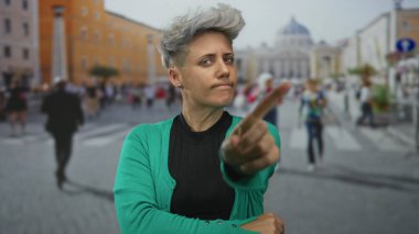 Kısa saçlı ve yeşil hırkalı bir kadın, barok cephesinin önündeki kalabalığın arasında parmakla işaret ediyor..