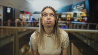 Bir alışveriş merkezinde neşeli bir şekilde poz veren, geçmişi bulanık, dükkanları ve ışıkları gösteren, canlı bir alışveriş merkezi atmosferi yakalayan bir kadın..