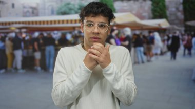 Kalabalık şehir pazarı sokak sahnesinde gözlüklü bir adam somurturken göğsünü sıkıyor; endişe gerginliği incinebilirlikten korkuyor.